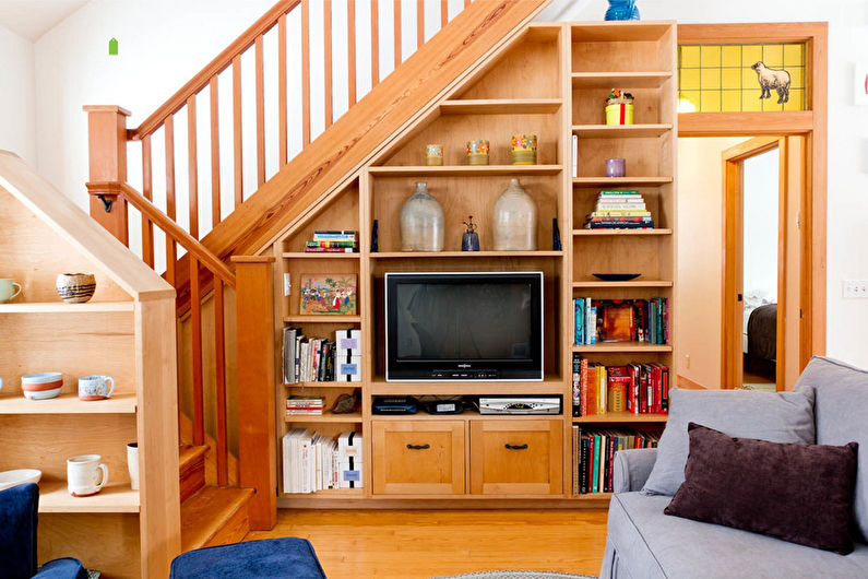 a living room with a tv and bookshelves under the stairs.