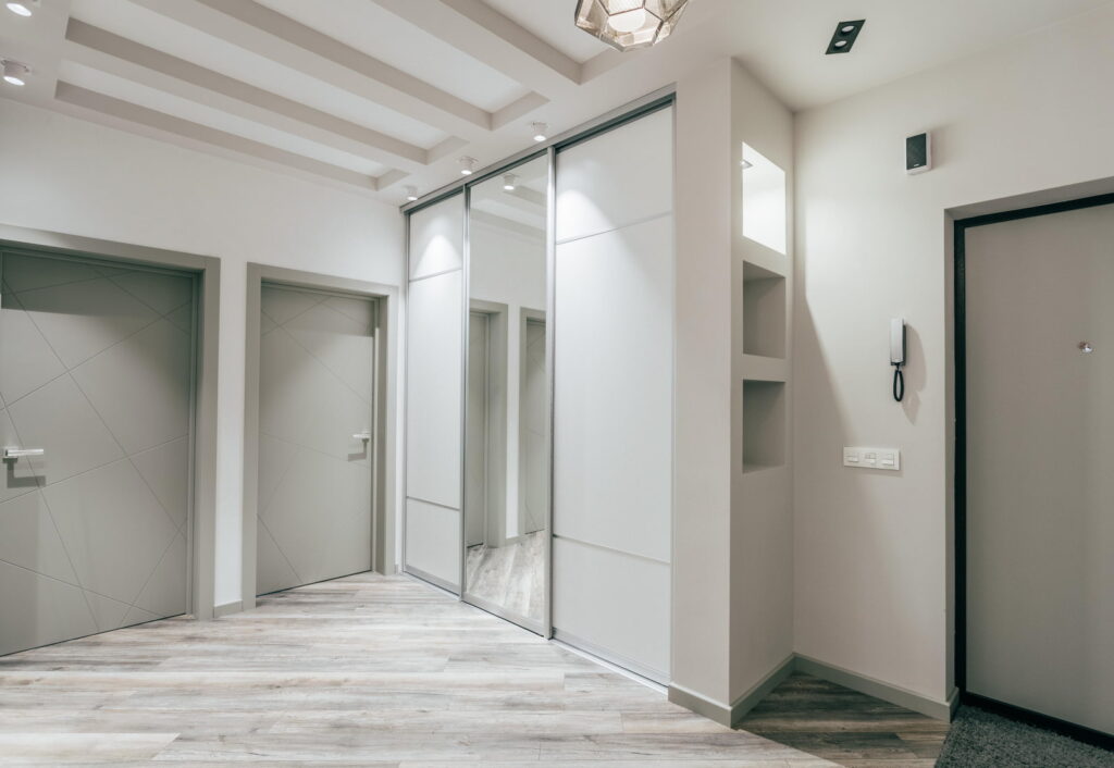 a hallway in a modern apartment with a door and mirrors.