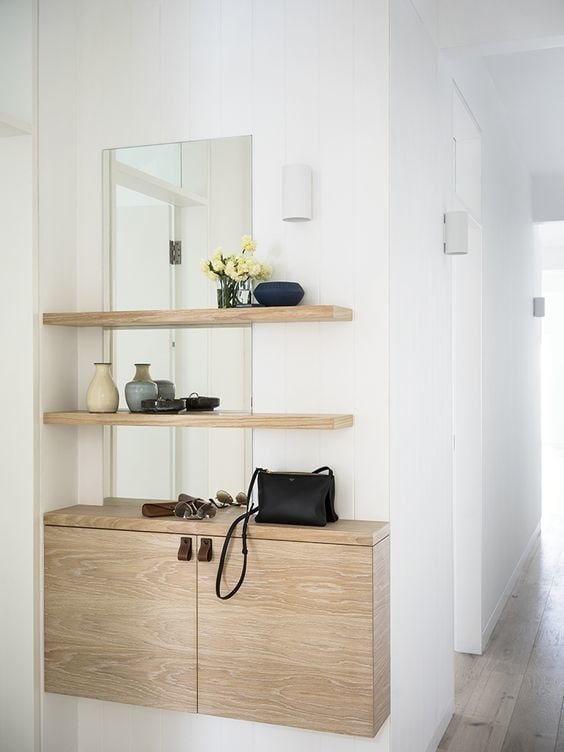 a white hallway with wooden shelves and a mirror.