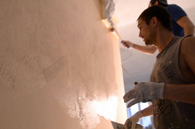 two men are painting a wall in a room.