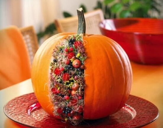 A pumpkin is sitting on a red plate with berries on it.