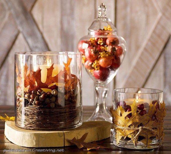 Three glass jars with fall decorations on top of a wooden table.