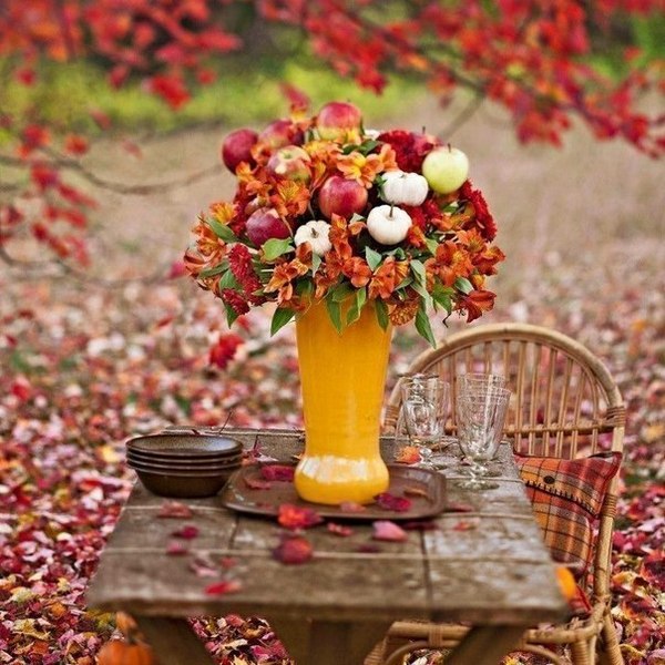 A table with a vase filled with fall flowers and apples.