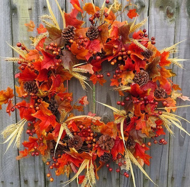 A wreath with fall leaves and berries hanging on a fence.