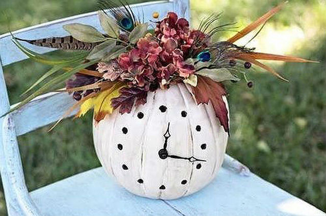 A clock sitting on a chair with flowers and feathers.