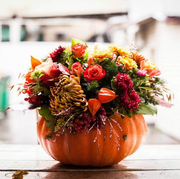 An arrangement of flowers in a pumpkin on a wooden table.