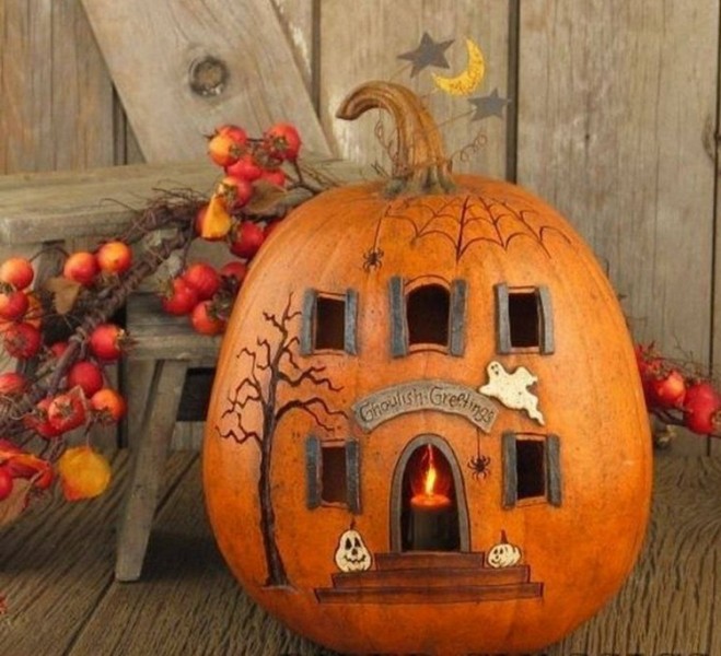 A pumpkin with a house on it sits on a wooden table.