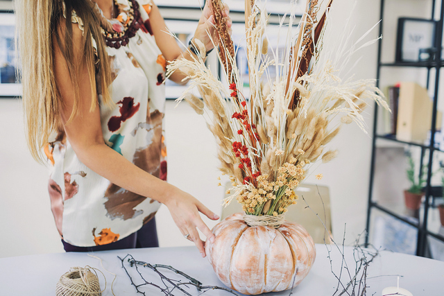 A woman is putting flowers in a vase on a table.