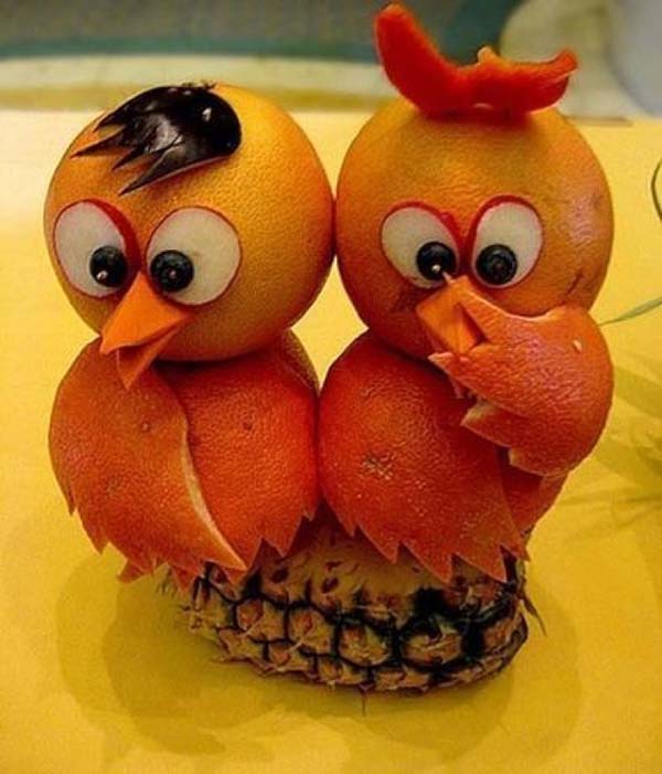 Two orange birds sitting on top of a pineapple.