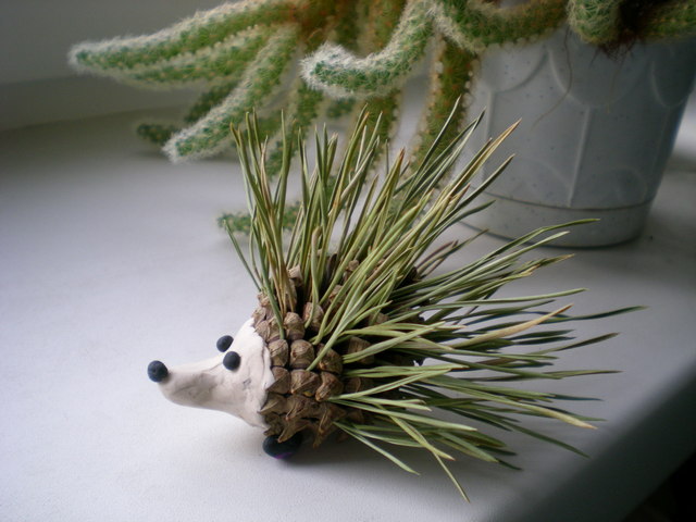 A small hedgehog on a table next to a cactus.