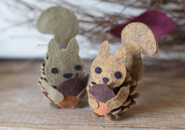 Two felt squirrels with acorns in their mouths.