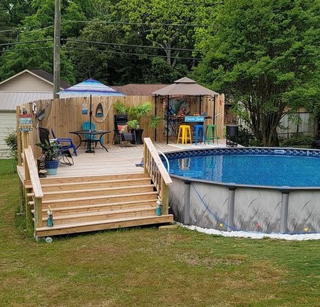 A backyard with a wooden deck and a swimming pool.