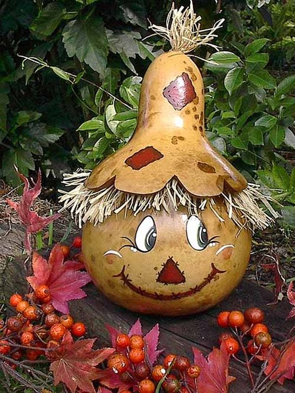 A pumpkin with a straw hat on it sits on top of a pile of leaves.