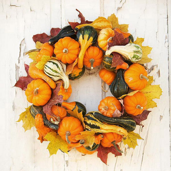 A wreath of pumpkins and gourds hanging on a white wall.