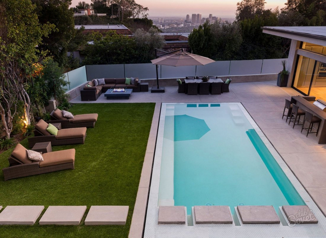 A modern backyard with a swimming pool and lounge chairs.