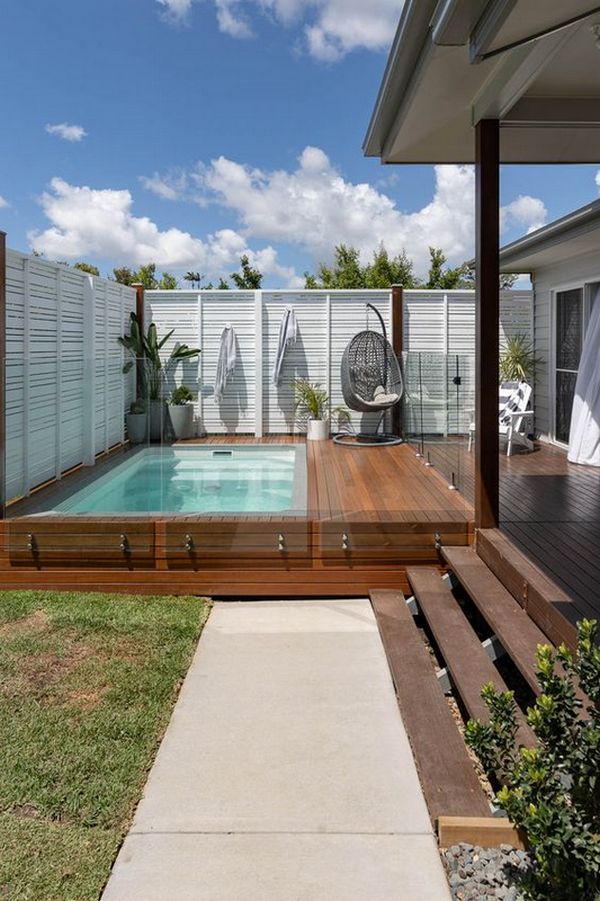 A backyard with a wooden deck and a swimming pool.