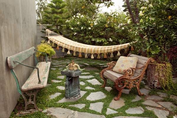 A hammock sits on a stone bench in a backyard.