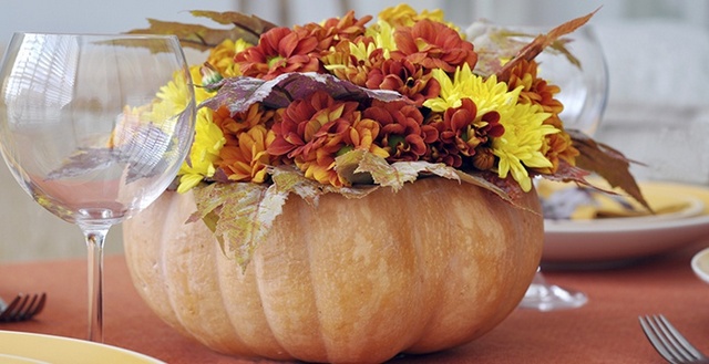 A pumpkin centerpiece with flowers on a table.