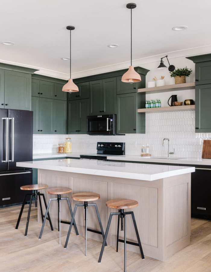 A kitchen with green cabinets and black stools.