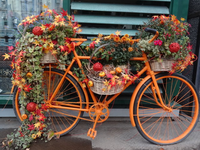 An orange bicycle decorated with flowers and leaves.