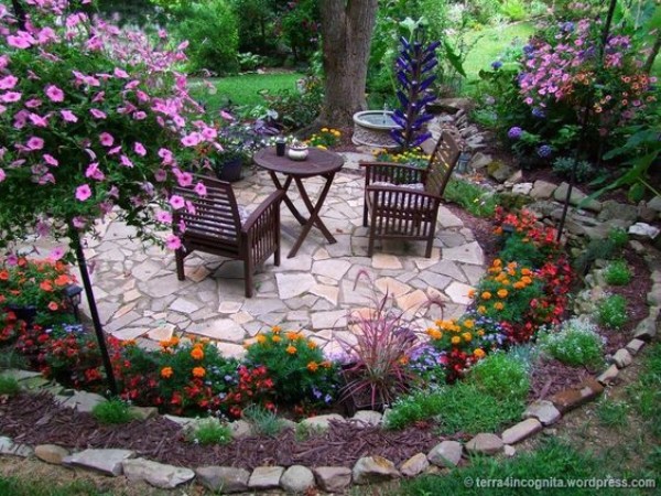 A garden with a stone patio and flowering plants.