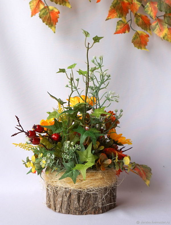 An arrangement of autumn leaves and flowers on a wooden stump.