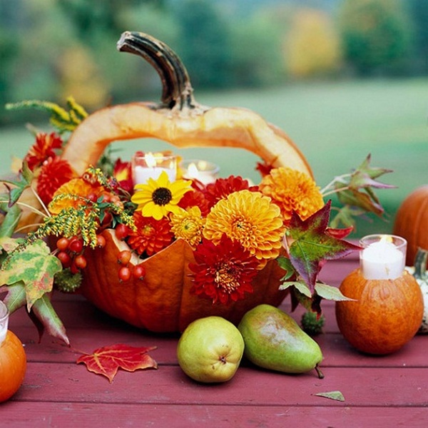 A pumpkin decorated with flowers and candles on a table.