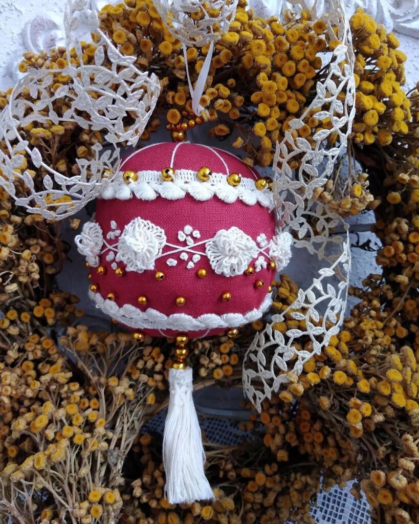 A red and white ornament hangs from a wreath of yellow flowers.