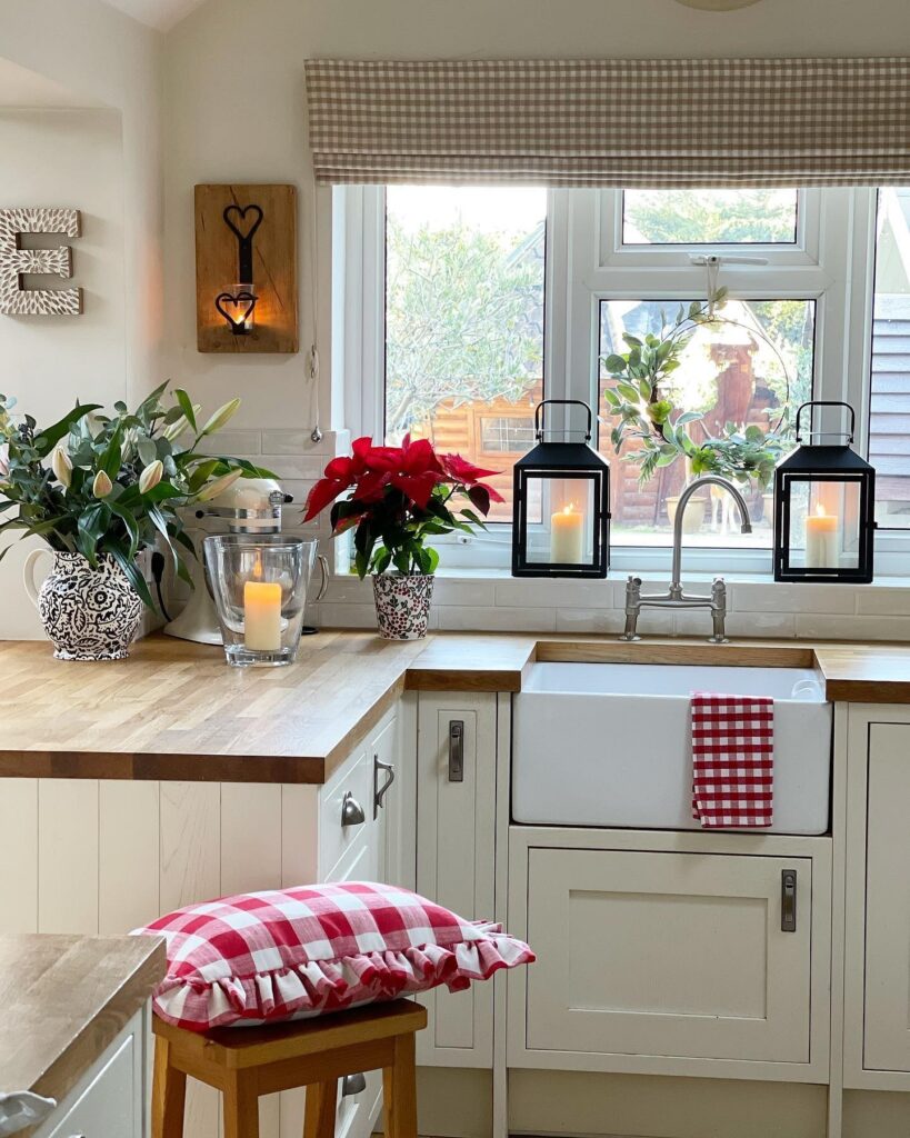 A white kitchen with red and white checkered stools and a window.