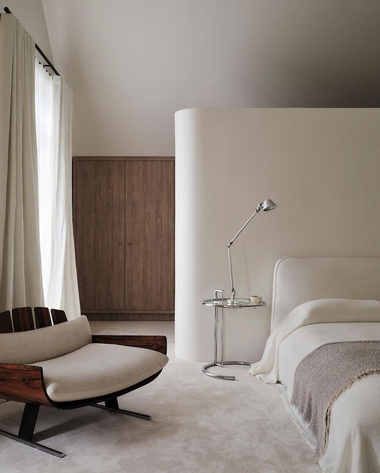 A white bedroom with a wooden bed and chair.