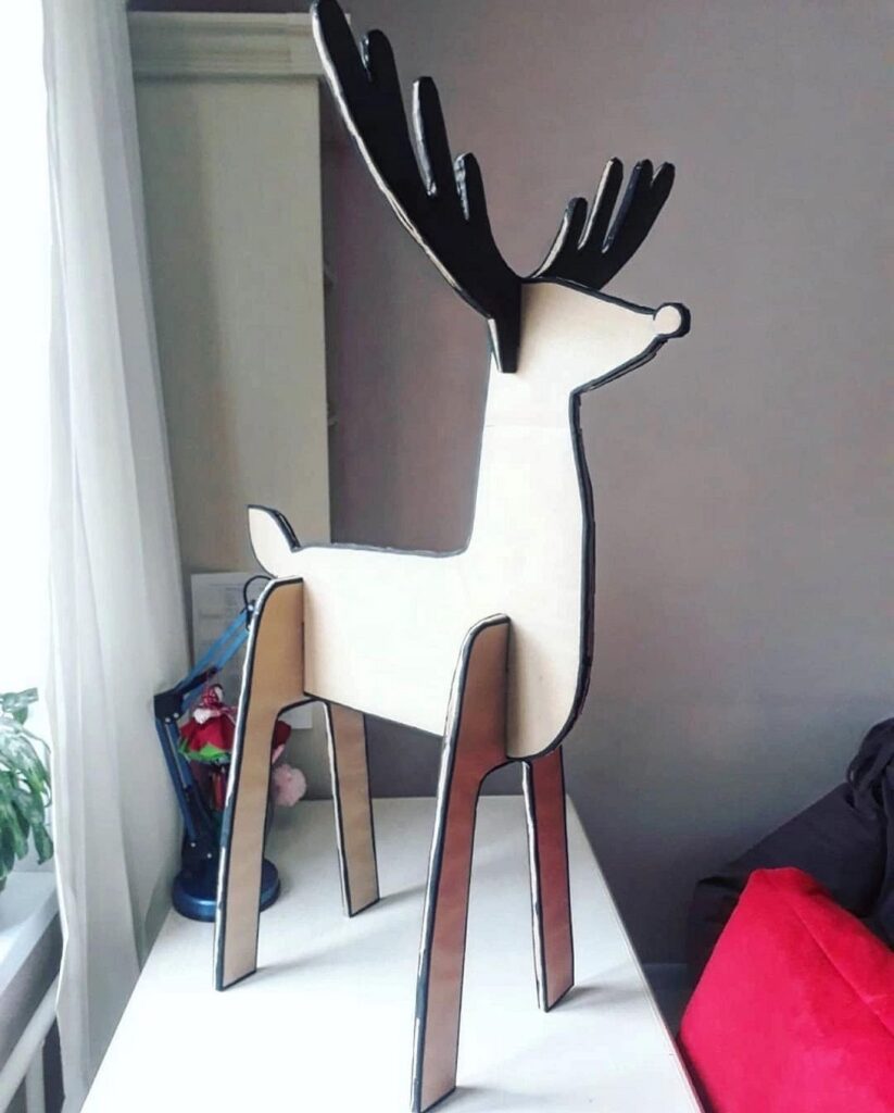 A wooden reindeer standing on a table in front of a window.