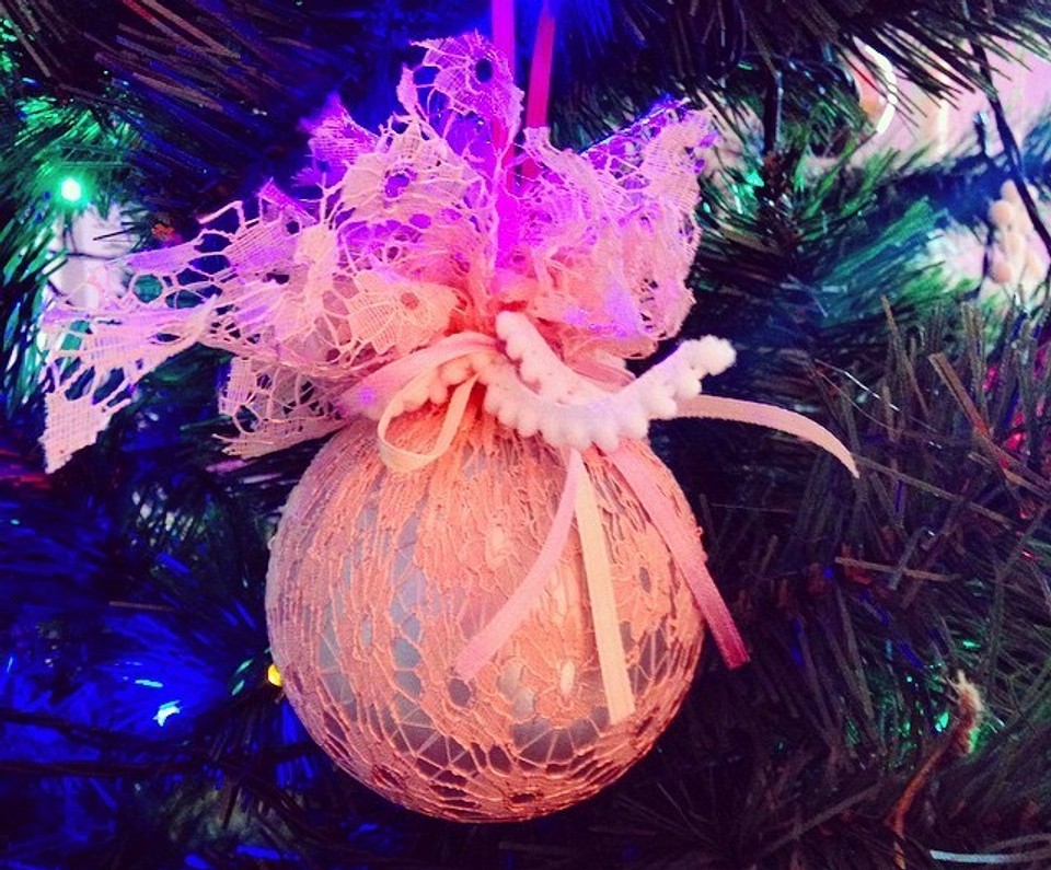 A pink lace ornament hanging on a christmas tree.