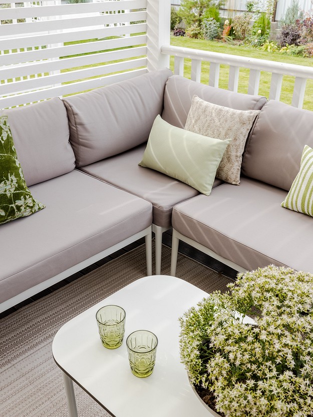 A white patio with a grey couch and green pillows.