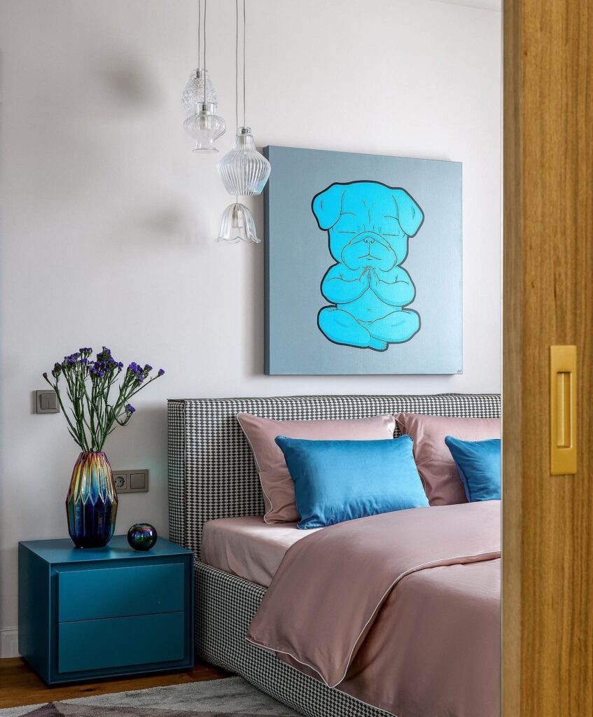A bedroom with a blue bed and a painting on the wall.