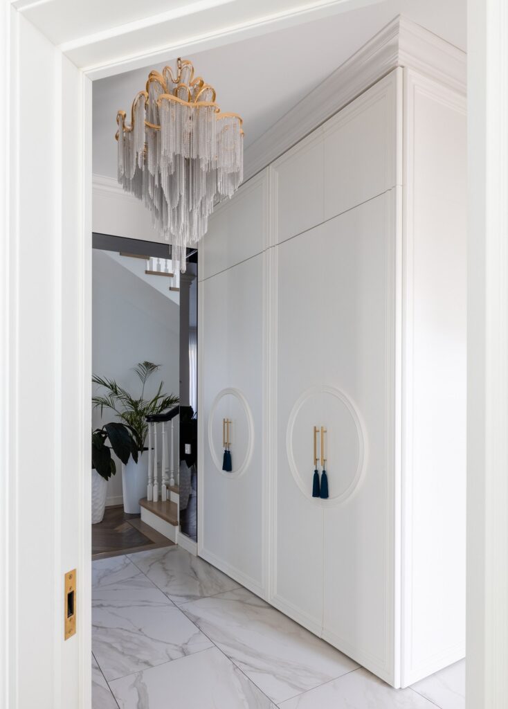 A white hallway with a chandelier and marble floor.