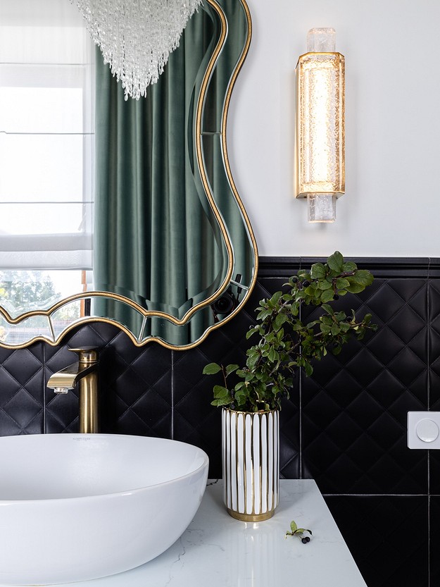 A black and gold bathroom with a gold mirror.