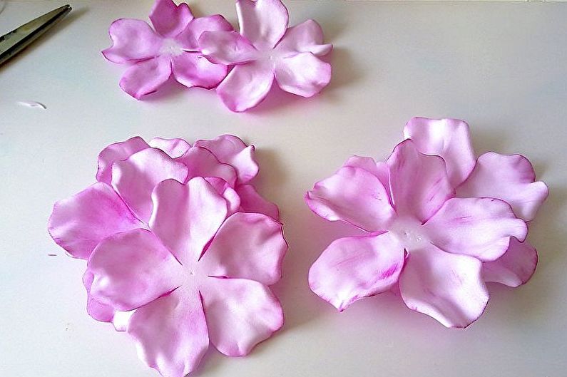 Three pink flowers with scissors on a white table.