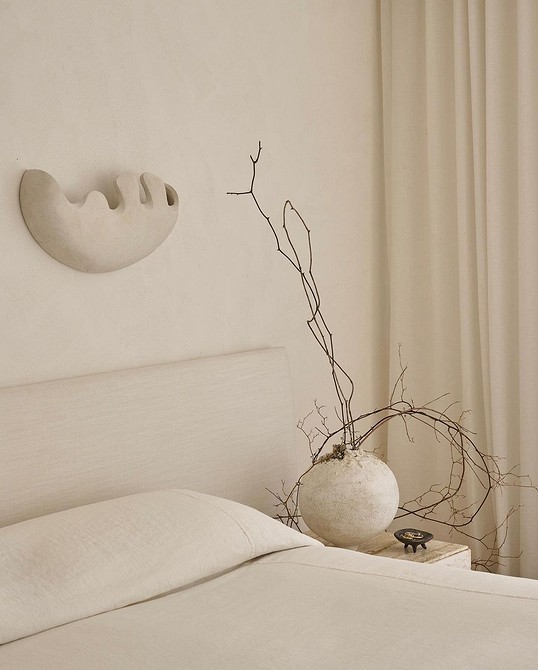 A bedroom with a white bed and a vase on the wall.