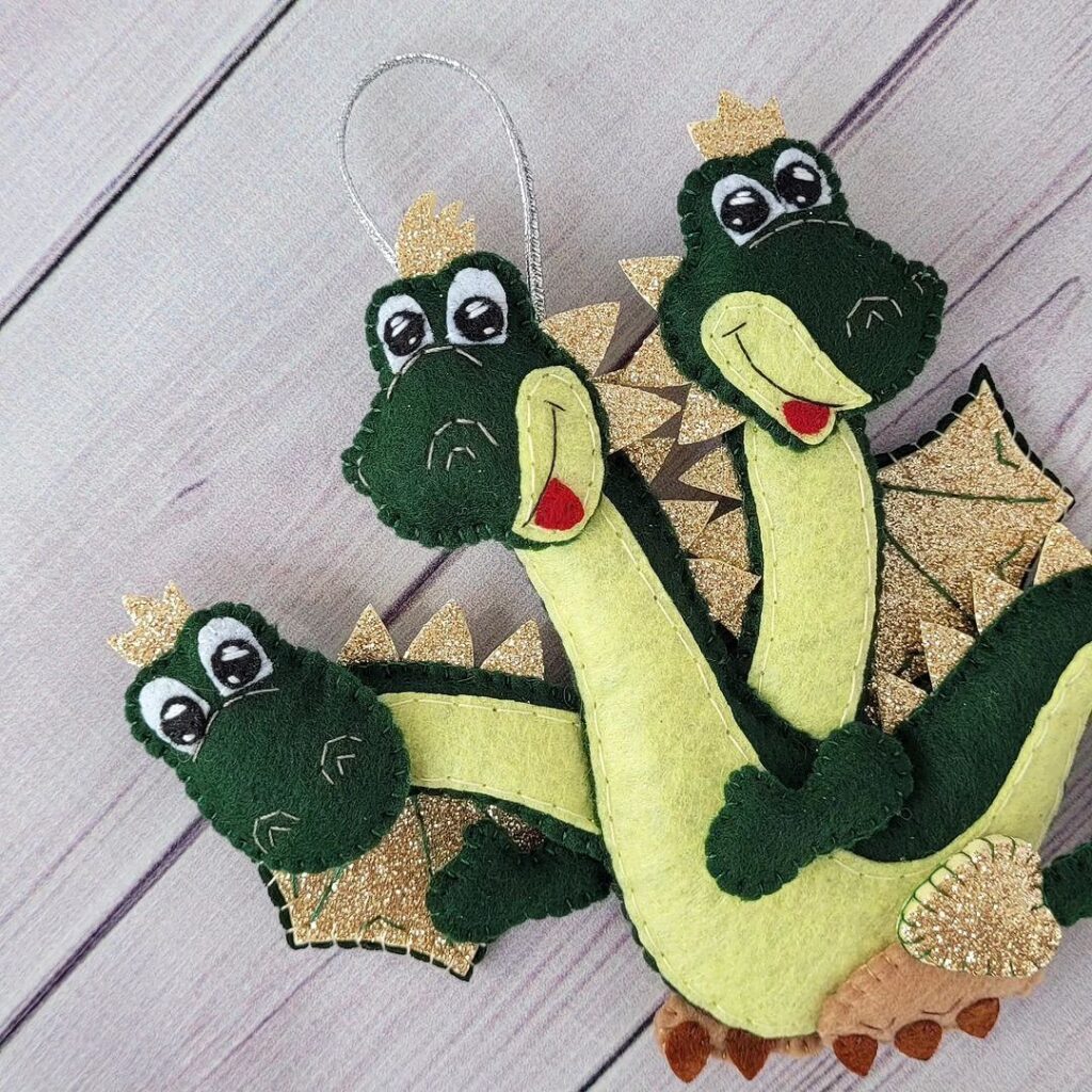 Three felt dragon ornaments hanging on a wooden surface.