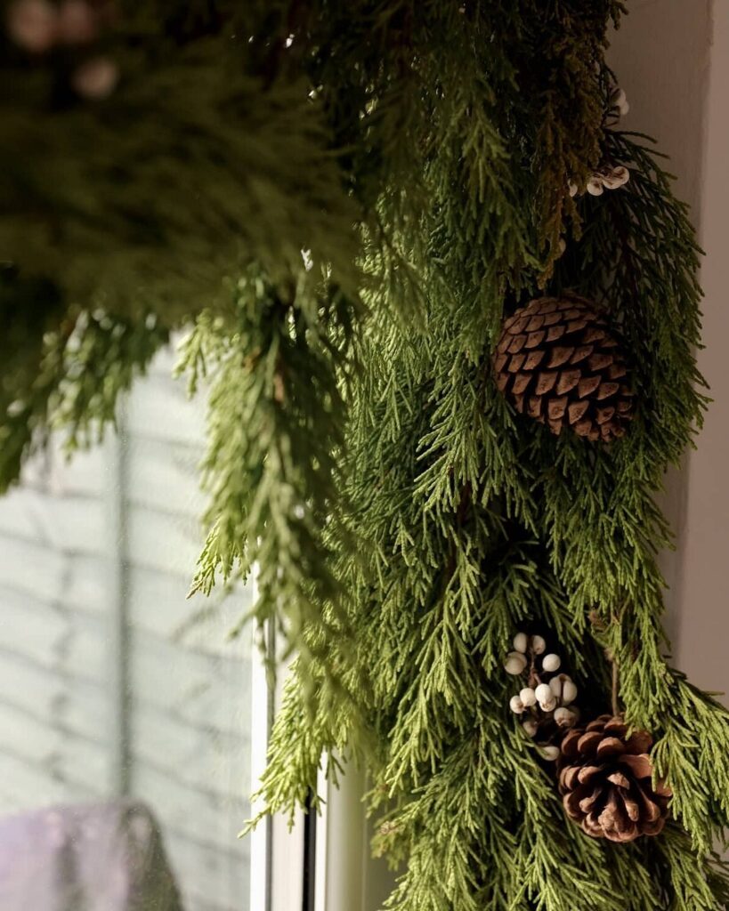 A christmas wreath hangs on a window sill.