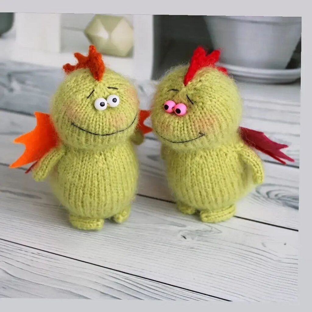 Two knitted green dragons on a wooden table.