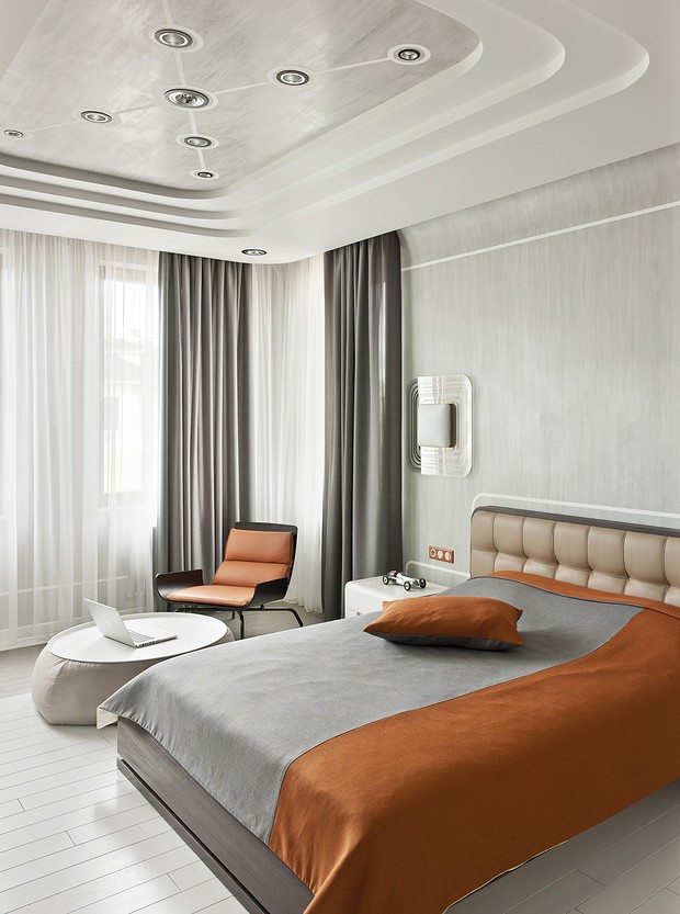 A modern bedroom with a white bed and orange accents.