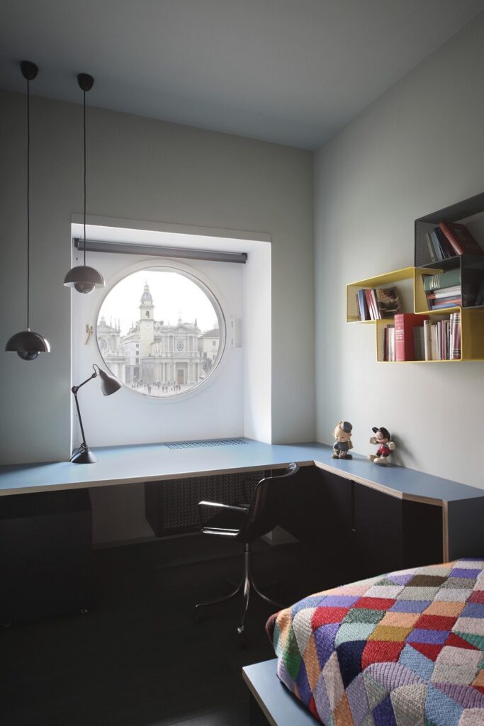 A bedroom with a round window and a colorful blanket.