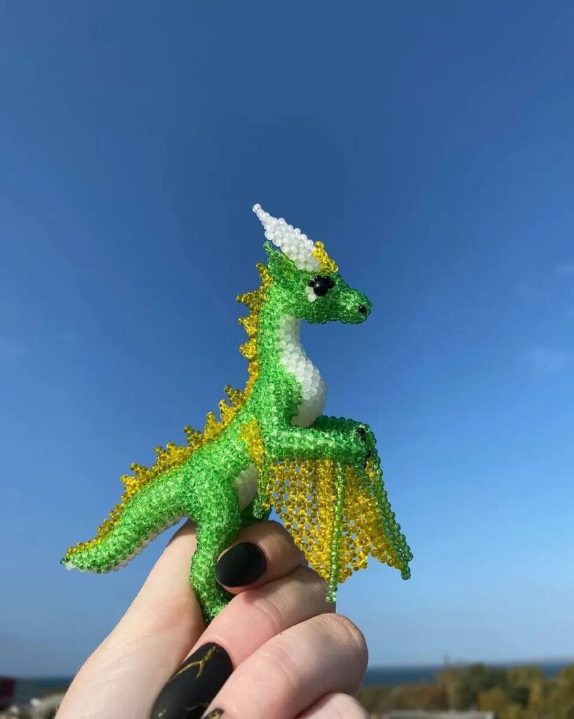 A person holding a green and yellow beaded dragon.