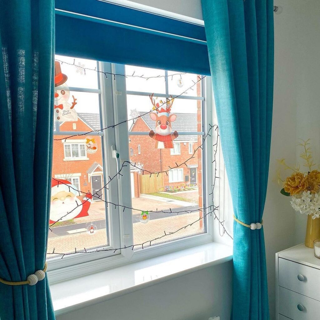 A bedroom with blue curtains and a window with santa decorations.