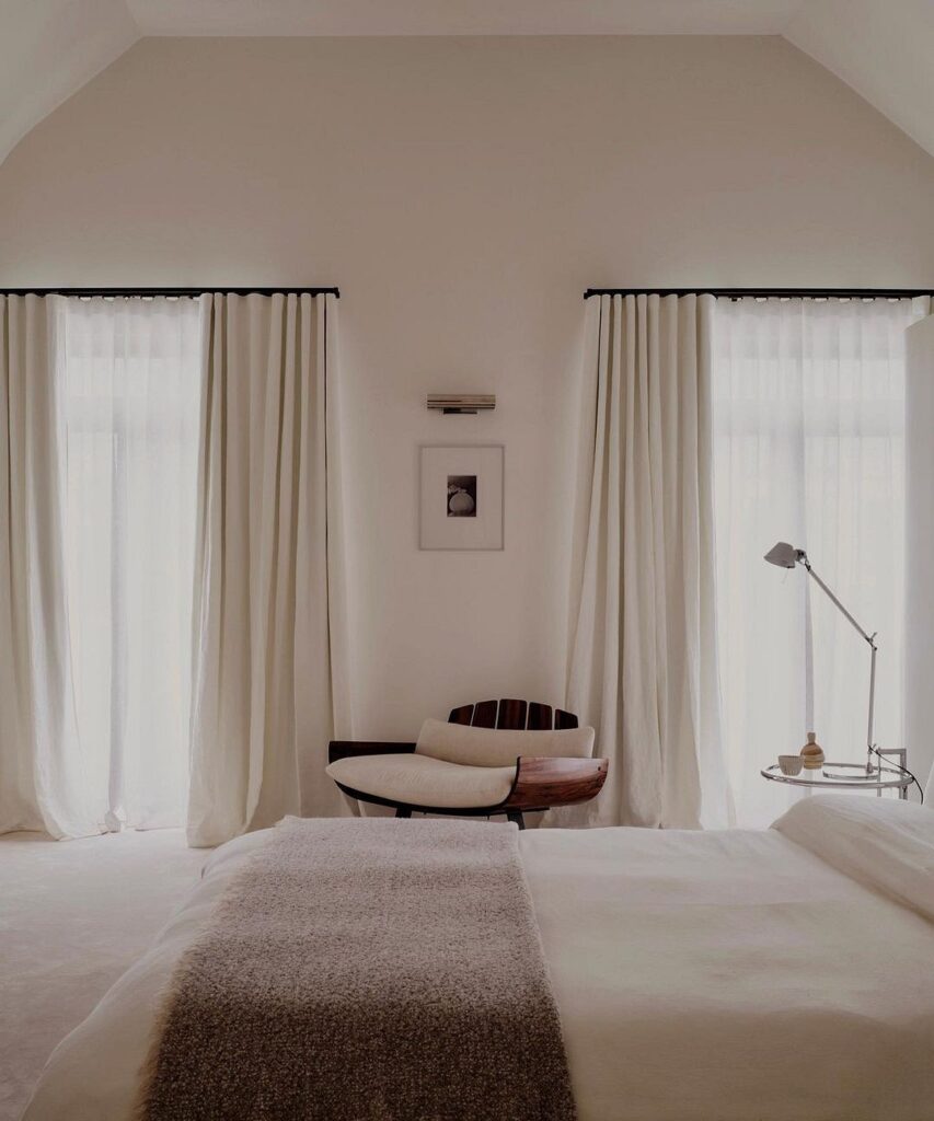 A bedroom with white curtains and a chair.