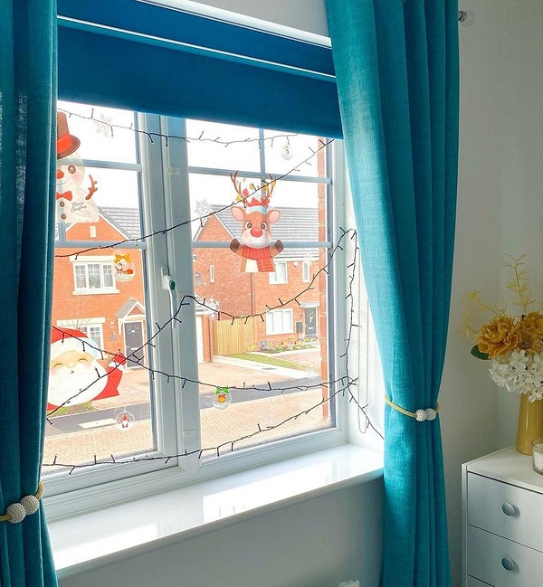 A bedroom with a window decorated with santa and reindeer.