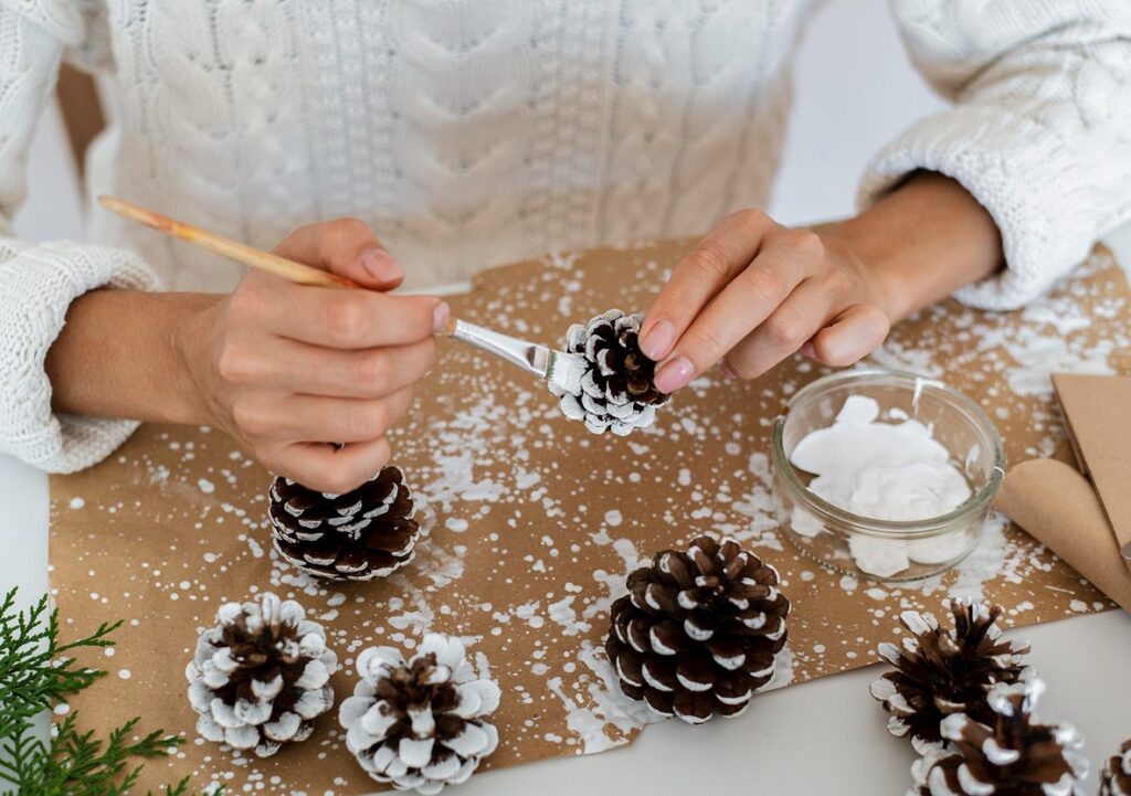 A woman is decorating pine cones on a table.