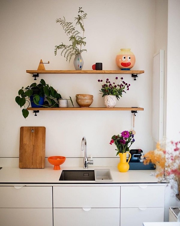 A white kitchen with wooden shelves and potted plants.