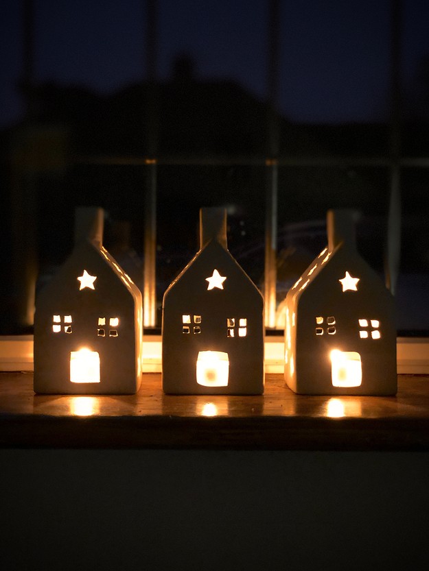 Three house shaped candle holders sitting on a window sill.